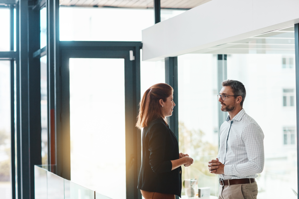 Two business people, a man and a woman, talking in a hallway - representing Nerve Strategic's Executive Presence