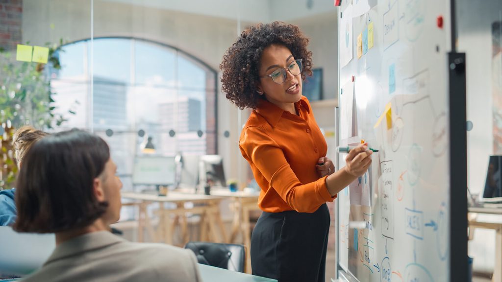 A confident woman writing on a white board - the image is to represent Nerve Strategic's Leadership Development